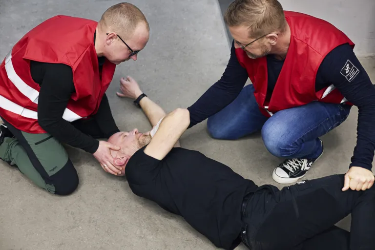 Deltagere øver håndtering af en person på gulvet under et førstehjælpskursus